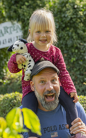 Der Papa trägt seine kleine Tochter durch den Irrgarten auf seinen Schultern.