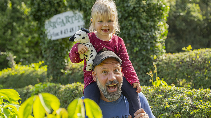 Der Papa trägt seine kleine Tochter durch den Irrgarten auf seinen Schultern.