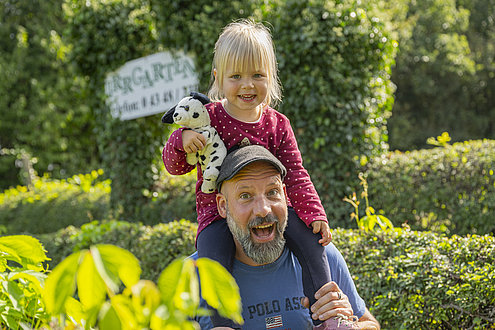 Der Papa trägt seine kleine Tochter durch den Irrgarten auf seinen Schultern.