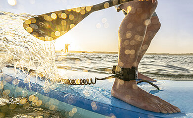 Füße auf einem SUP, das Wasser spritzt ans Brett und im Hintergrund der Horizont und das Meer
