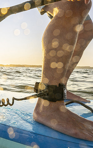 Füße auf einem SUP, das Wasser spritzt ans Brett und im Hintergrund der Horizont und das Meer