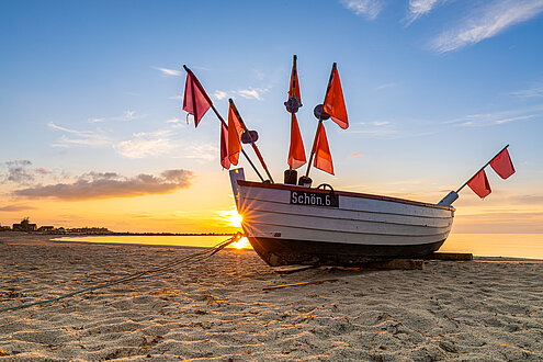 Ein Boot liegt auf dem Strand in Schönberg, es ist Abendlicht und der Himmel färbt sich rosa.