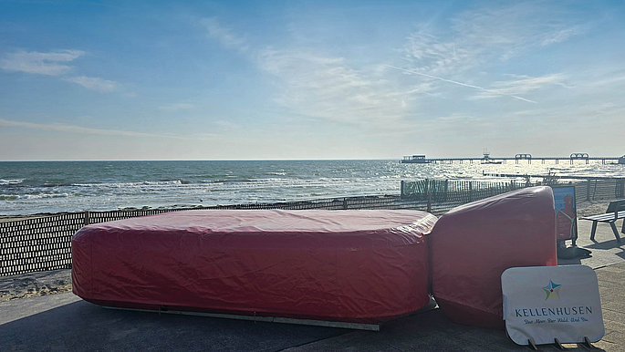 Eine riesige rote Wärmflasche liegt am Ostseestrand. 