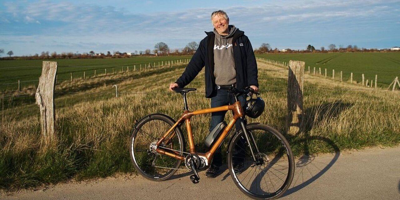 Axel Kramer steht mit seinem Fahrrad auf der Landstraße. Hinter ihm sieht man die Felder.
