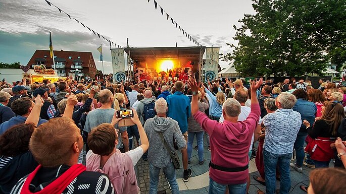 Viele Menschen vor einer Bühne, sie heben die Hände und tanzen. 