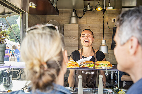 Eine lachende Frau übergibt Fischbrötchen an Gäste