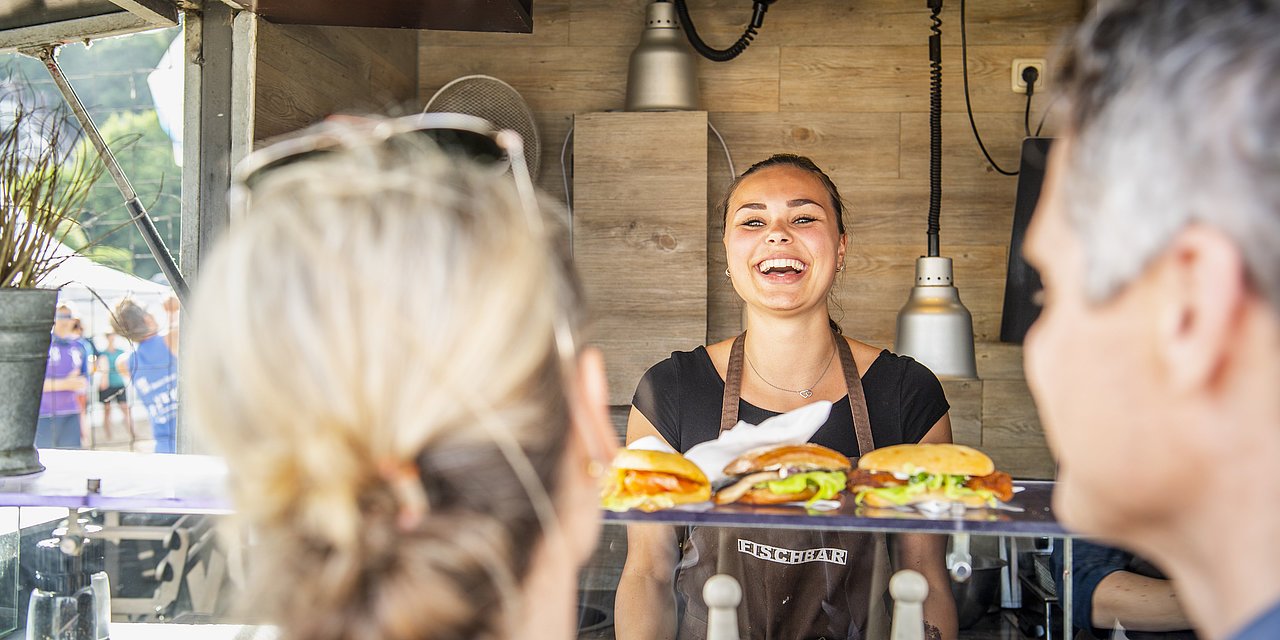 Eine lachende Frau übergibt Fischbrötchen an Gäste