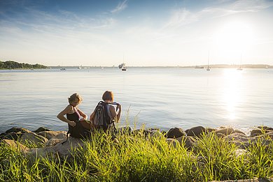 Zwei Freundinnen wandern entlang der Steilküste und setzten sich für eine kleine Pause an den Rand der Steilküste und genießen den Ausblick auf die Ostsee.