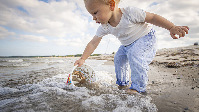 Ein kleines Kind am Strand, taucht ein Spielzeug ins Wasser.