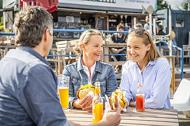 Drei freunde sitzen vor einer Fischbrötchenbude und essen ein Fischbrötchen