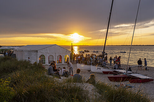 Über dem Campingplatz Grönwohld geht die Sonne unter. Am Strand ist ein großen weißes Zelt aufgebaut.