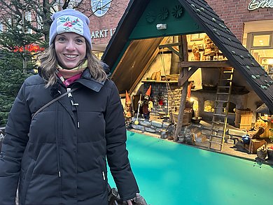 Frau vor einer gebauten Hütte aus Holz, in der kleine Zwerge arrangiert sind. 