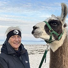 Eine Frau mit zwei Lamas am Strand.