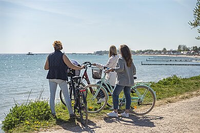 Drei Radfahrende machen Halt und schauen auf das Meer. 