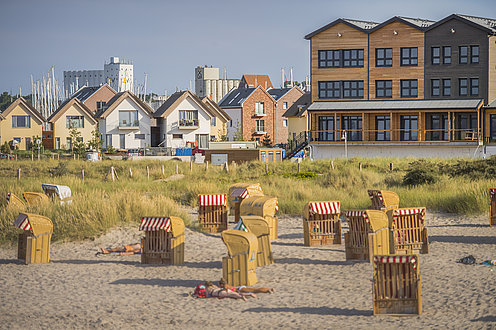 Im Vordergrund ist der Strand mit einzelnen Strandkörben, die unterschiedlich ausgerichtet, zu sehen. Im Hintergrund sind Hotels und Ferienwohnung von Heilgenhafen zu sehen.