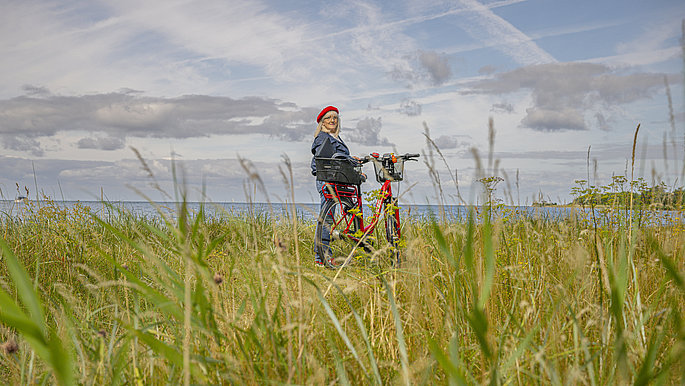 Eine Frau mit ihrem Rad zwischen Wiesen und Meer auf Fehmarn an der Ostsee. 