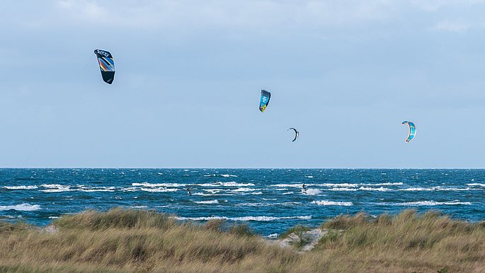 Einige Personen Kiten. Die Kites sind im blauen Himmel zu sehen.