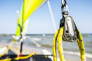 Im Hintergrund das Meer, im Vordergrund sind nur ausschnitthaft Ringe mit Seilen erkennbar, die zu einem Segelboot gehören. 
