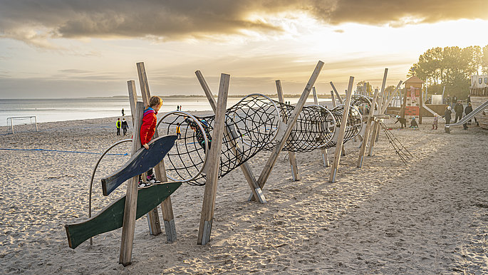 Am Strand von Großenbrode ist ein Kinderspielgerät zu sehen. Das Spielgerät stellt ein langes rundes Fischnetz da. In der Mitte sind "Fische" zusehen, die durch das Netz schwimmen.