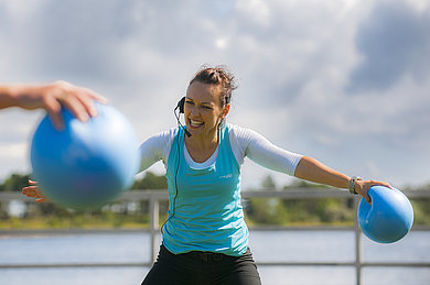 Eine Trainerin zeigt eine Übung mit einem glauben Ball.